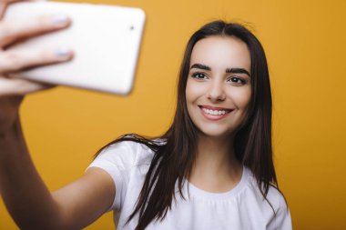 Şaşırtıcı genç kadın esmer bir selfie önünde sarı arka plan gülüyor smartphone ile yapıyor.