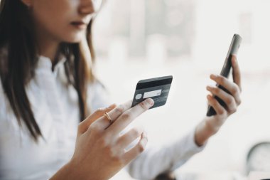 Başka bir elinde kapalı bir akıllı telefon ise plastik bir kredi kartı tutan kadının ellerini yan görünümü.