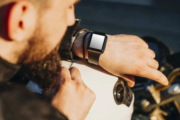 Hand with smart watch of a young bearded biker sitting on his bi