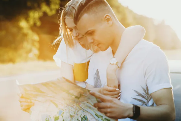 Porträt eines schönen Paares, das sich umarmt und in eine Landkarte blickt, während — Stockfoto