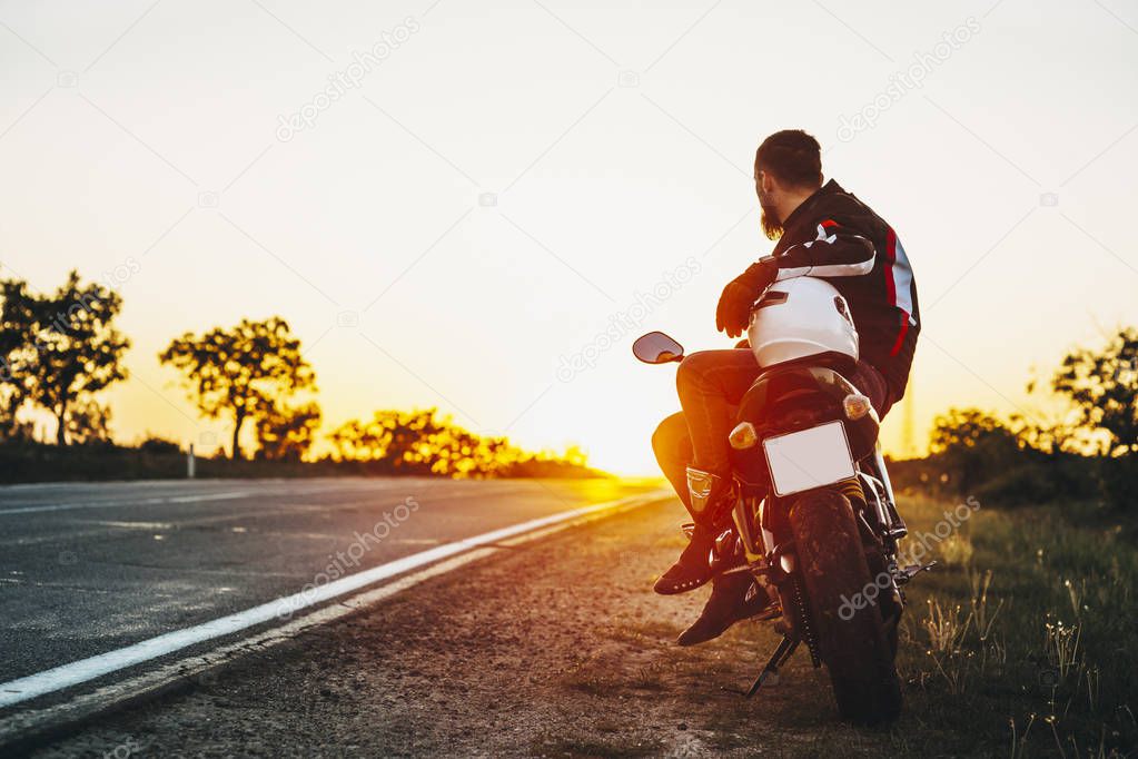 Back view of a bearded biker sitting on his motorcycle sitting a