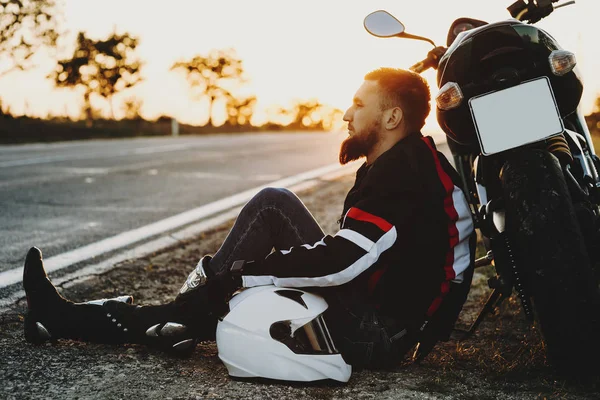Confiante adulto masculino motociclista sentado no chão perto da estrada l — Fotografia de Stock