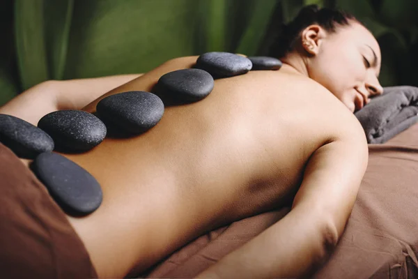 Female back with hot volcanic stones while having hot stones therapy in a wellness spa center.