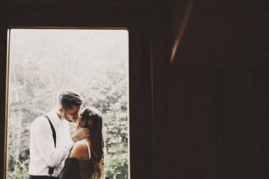 Damat takım elbise giymiş iken bir sevgi genç evli çift balkonda öpüşme Yan görünüm portre sadece omuzlarında bir battaniye ile eşi ise.
