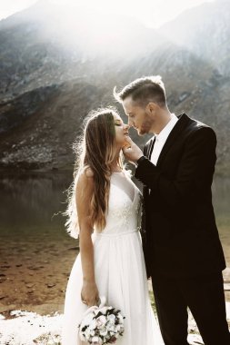 Sabahgöl ve dağa karşı öpüşmeden önce birbirlerine gülümseyen genç ve sevimli beyaz bir çiftin yan görünüm portresi.