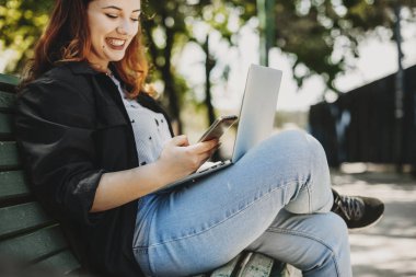 Gülümseyen bir akıllı telefon kullanarak bir bankta oturan bir vücut pozitif kadın Eller .