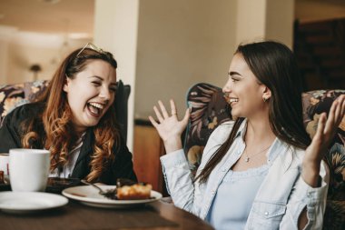 Uzun saçlı hikaye anlatımı ile güzel genç esmer bir kahve dükkanında otururken gülüyor kız arkadaşı için el hareketleri kullanarak bir şey.
