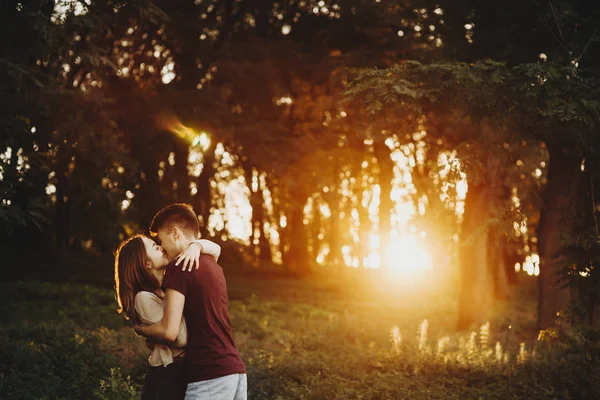仕事の後を歩きながら公園の夕日の光に抱き合い 抱きしめる素晴らしいカップル — ストック写真