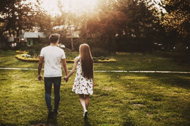 Arka görüş çift gün batımına karşı yürürken parkta el ele uzanan.