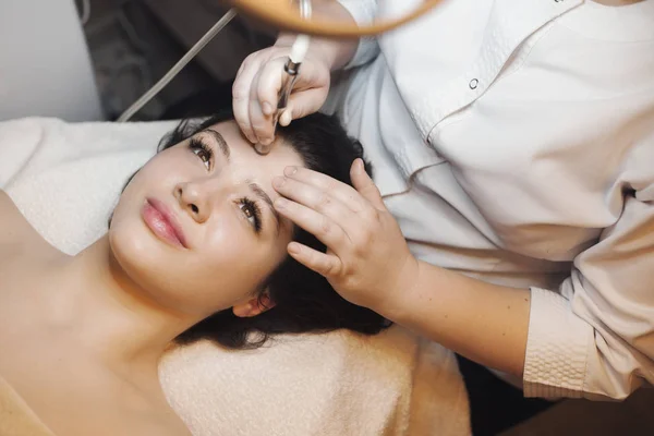 Upper view of a lovely caucasian female having a facelift procedures on her face leaning on a spa bed with open eyes .