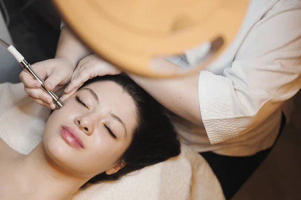 Upper view portrait of a attractive woman having a lifting therapy on her face by a cosmetician with a lifting device.