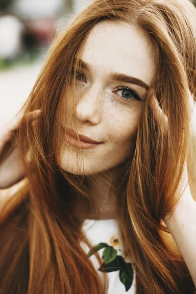 特写一个惊人的红头发的女孩与雀斑和绿色的眼睛看着相机微笑触摸她的红头发外面 — 图库照片