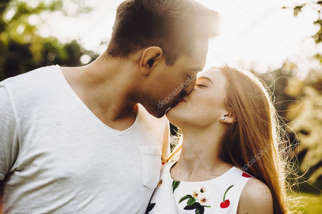 Side view portrait of a beautiful young caucasian couple kissing against sunset while dating outside in nature.