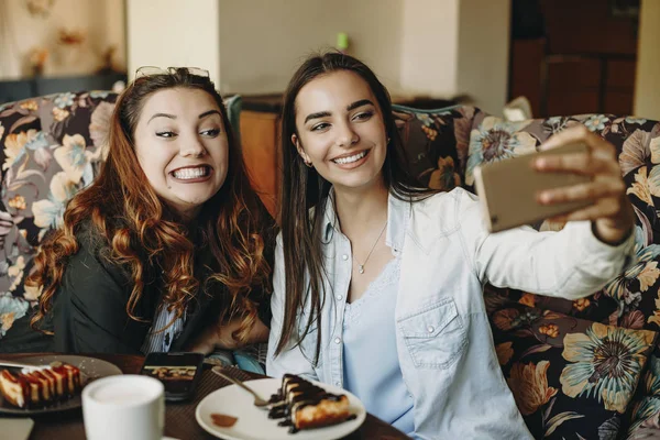 Zwei erstaunliche junge Freundinnen machen im Sitzen ein lustiges Selfie — Stockfoto