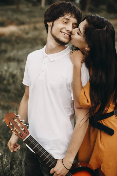 Jovem encantador segurando uma guitarra e rindo enquanto é beijada — Fotografia de Stock