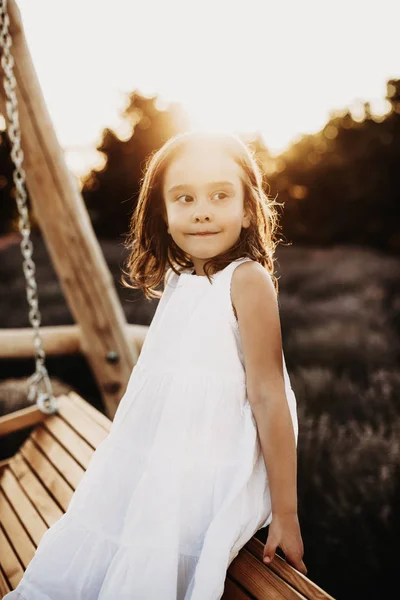 Retrato de uma menina bonita sentada em um balanço de madeira olhando — Fotografia de Stock