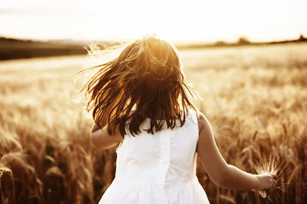 Menina irreconhecível correndo em um campo de trigo contra sóis — Fotografia de Stock
