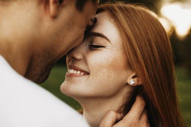 Close up side view portrait of a lovely female with freckles and red hair smiling with closed eyes before kissing while her boyfriend is touching her hair clipart