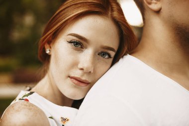 Çekici kızıl saçlı, çilli, gri gözlü, kameraya ciddi ciddi bakan bir kadının portresini yakından çek. Kafasını dışarıda erkek arkadaşının arkasına yaslarken..