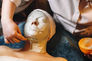 Kozmetik uzmanı kadın yüzüne aljinat maskesi takıyor.