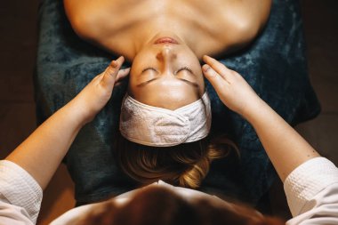 Kozmetik uzmanı elleri beyaz bir adama yüz masajı yapıyor.