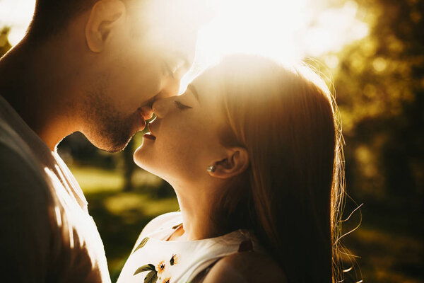 Side view portrait of a amazing caucasian couple kissing against the sunset with closed eyes white woman with freckles and red hair is smiling outside .