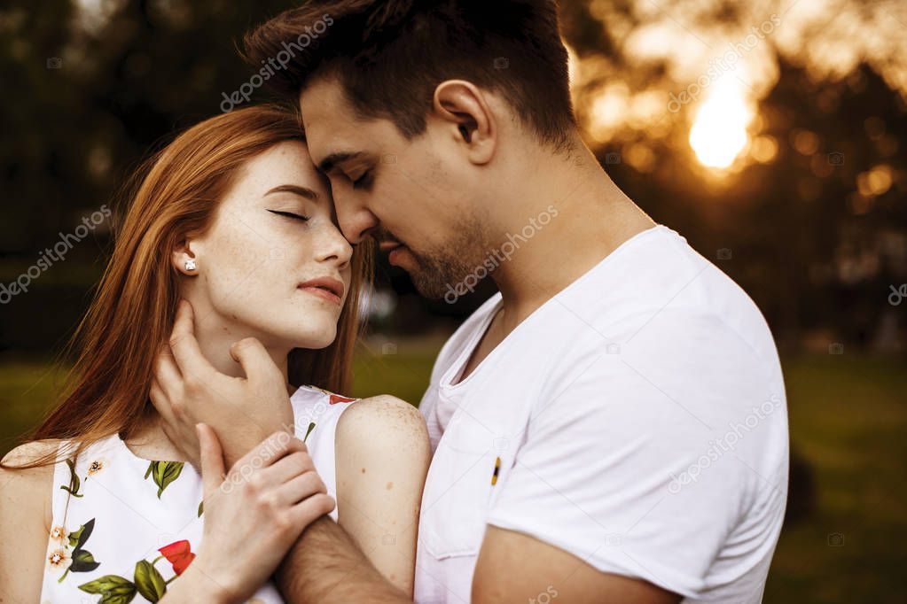 Side view portrait of a lovely caucasian couple embracing before kissing against sunset with closed eyes outside.