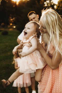 Gün batımına karşı annesinin kollarında uçarken gülen küçük tatlı kız. Genç ve güzel bir kadın kızıyla parkta oynaşıyor..
