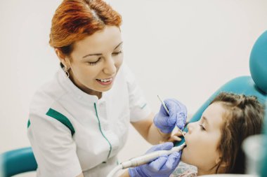 Genç sevimli pediatrik dişçi bir çocuğun dişlerini doldururken çalışıyor..