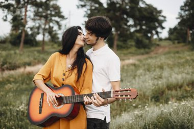 Doğada gitar çalan romantik genç bir çiftin portresi. Öpüşmeden önce birbirine bakan genç bir çift..