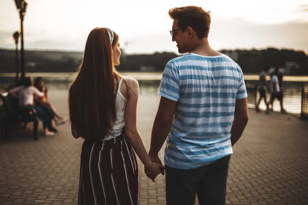 一对年轻貌美的年轻夫妇在日落前在公园散步时的后视镜 浪漫的男人和女人牵着手约会 彼此凝视 — 图库照片