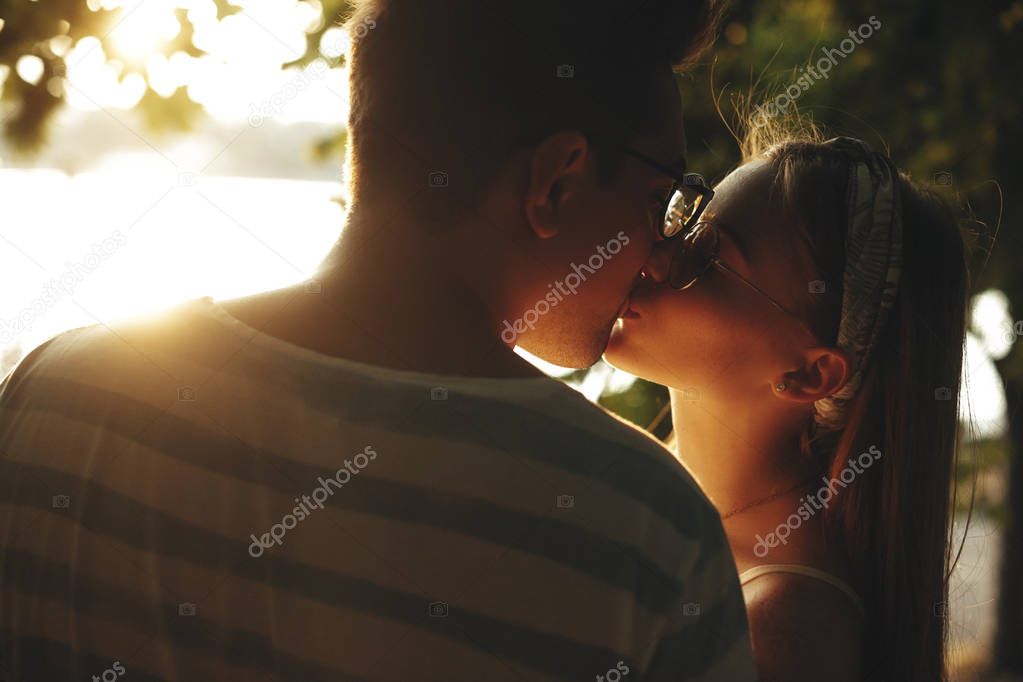 Close up portrait of a young cheerful couple kissing against sun
