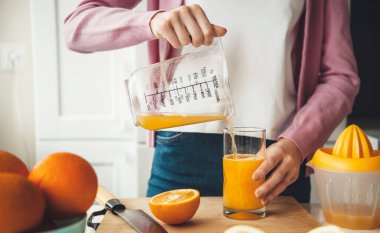 Kafkasyalı kadın mutfakta sıkacağı kullandıktan sonra bardağa taze portakal suyu koyuyor.