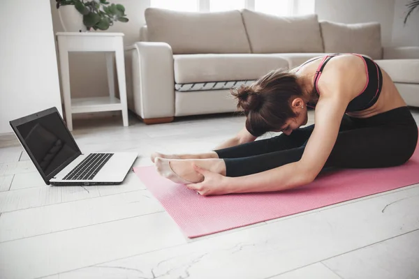 Foto vista laterale di una signora caucasica che fa yoga sul pavimento e utilizzando un computer portatile durante lo stretching — Foto Stock