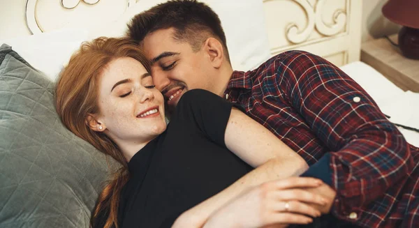 Ginger girl with freckles lying in bed with her lover embracing and smiling together — Stock Photo, Image