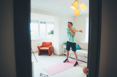 Kameranın önünde ısınan beyaz bir adam online spor salonu seansı yapıyor.