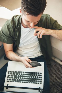 Evde bilgisayar ve telefonla çalışan genç bir girişimci.