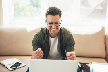 Gözlüklü genç işadamı bir kitap ve bazı belgelerle çalışırken bilgisayarında toplantı yapıyor.