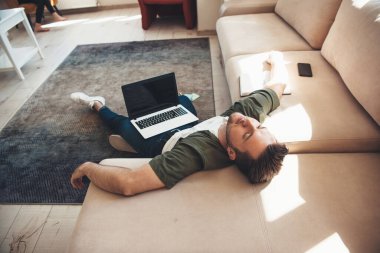 İnternette çalıştıktan sonra laptopuyla yerde yatan yorgun beyaz adam.