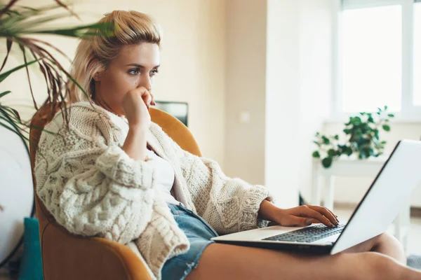Estudiante aburrido con el pelo rubio en suéter de punto sentado en el ordenador y el trabajo a distancia — Foto de Stock
