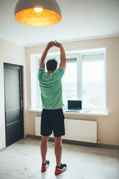 Alto hombre caucásico estirando su cuerpo y practicando la aptitud en casa mirando el portátil — Foto de Stock