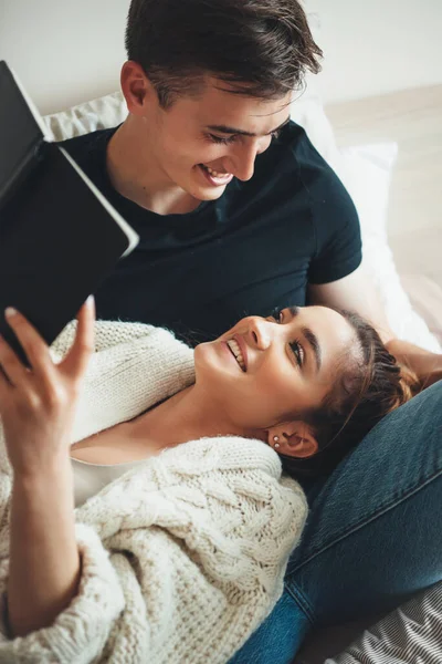 Preciosa mujer caucásica acostada sobre su amante mientras lee el libro y le sonríe mirando a los ojos y vistiendo un suéter de punto —  Fotos de Stock