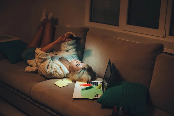 Cansado estudiante caucásico charlando por teléfono mientras está sentado en el sofá después de hacer la tarea tarde por la noche — Foto de Stock