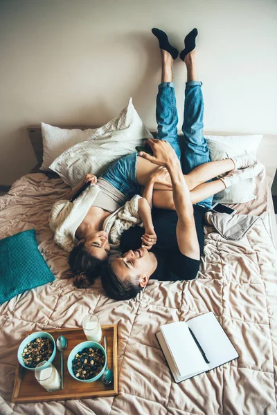 Charmant couple couché au lit avant de manger des céréales avec du lait près d'un livre ouvert — Photo