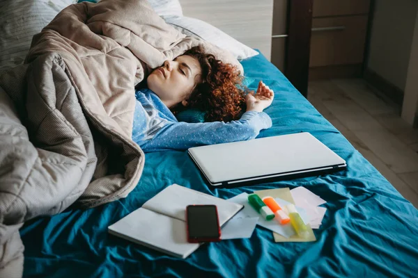 Caucásica chica con el pelo rizado quedarse dormido en su cama cubierta con una colcha después de hacer la tarea con su ordenador portátil — Foto de Stock