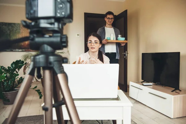 Cute caucasian woman having online lessons is explaining something while her lover is brinking the breakfast — Stock Photo, Image