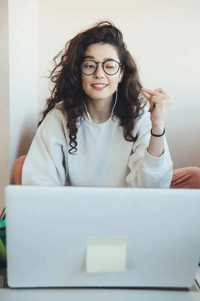 Lockig kvinna med glasögon och hörlurar som har en online lektion med hjälp av en dator hemma — Stockfoto
