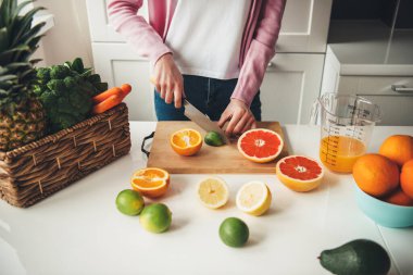 Evde taze meyve suyu yaparken masada meyve dilimleyen genç bir ev hanımı.