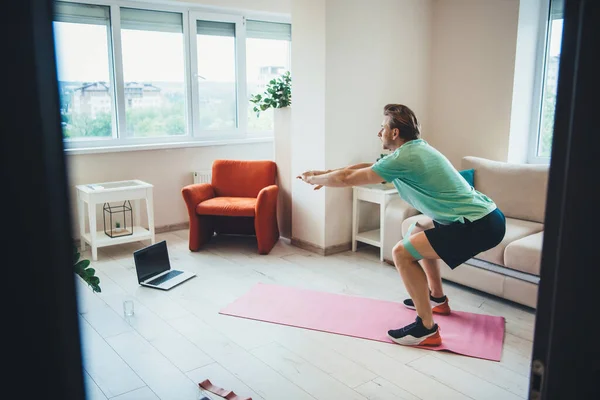 Uomo caucasico riscaldamento a casa mentre ha lezioni remote di fitness con un computer portatile — Foto Stock