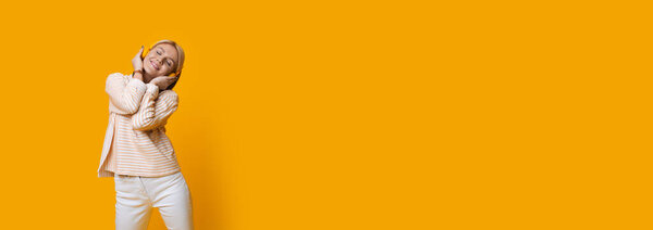 Очаровательная блондинка, слушающая размышления через наушники на желтой стене студии с бесплатным пространством
